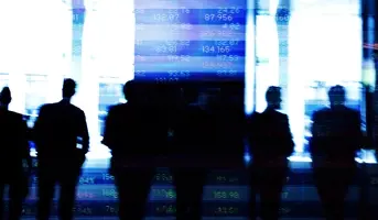 Silhouttes of people stood infront of abstract financial listings board