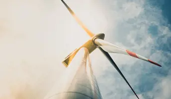 White and red wind turbine tower and blades taken from the base of the tower with cloudy blue sky in background