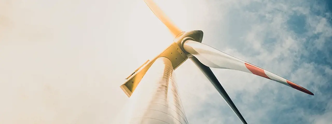 White and red wind turbine tower and blades taken from the base of the tower with cloudy blue sky in background