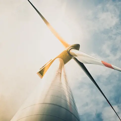 White and red wind turbine tower and blades taken from the base of the tower with cloudy blue sky in background