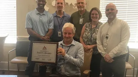 Group of five men and one woman with one man holding award plaque